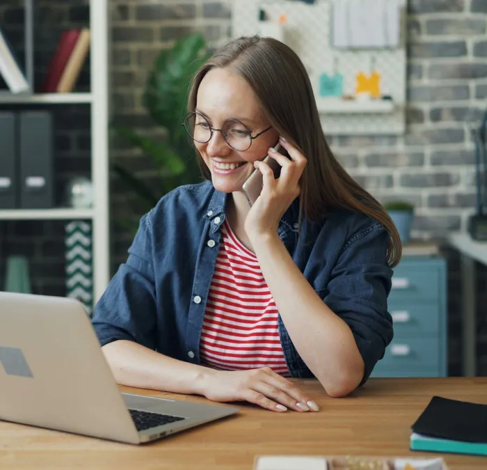 A woman smiling as she talks with a customer on the phone at her desk.