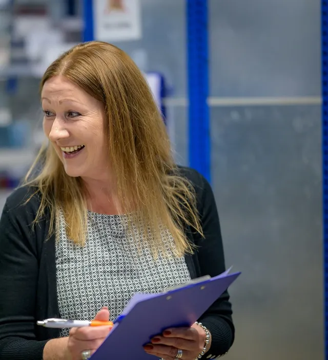 A business owner laughing during a conversation with a customer, clipboard in hand.